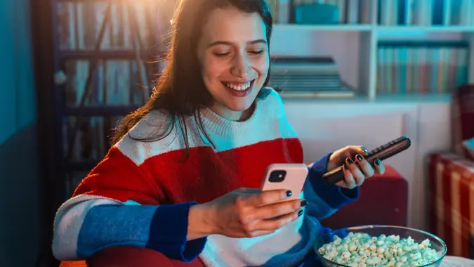 Woman using a phone while watching TV at home stock photo