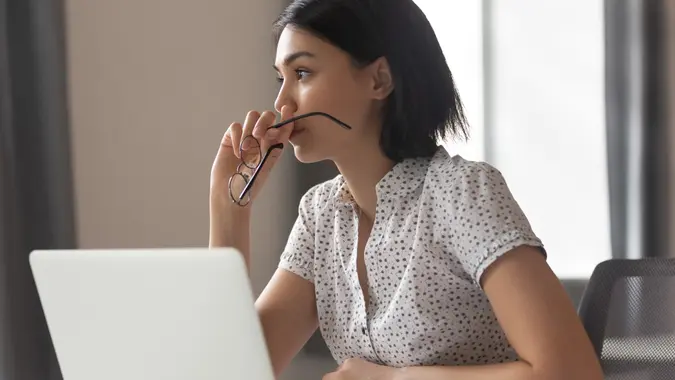 A focused Asian woman in business wear, her brow slightly furrowed as she concentrates on solving a difficult problem.