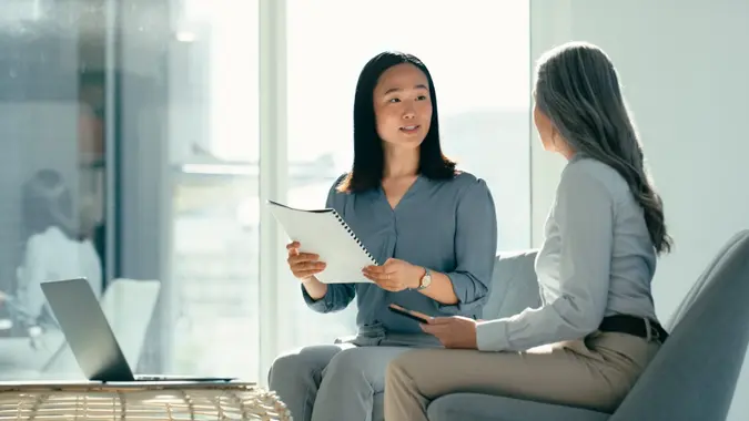 Two young women sitting together going over paperwork with a laptop in front of them.