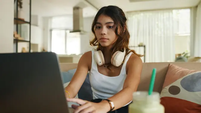 Young woman typing on laptop to make budget, learn new skills, do remote work, and other tasks.