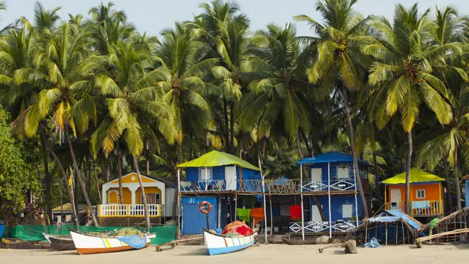 Fishing boats in front of a row of homes with palm trees all around on Palolem Beach Goa India.