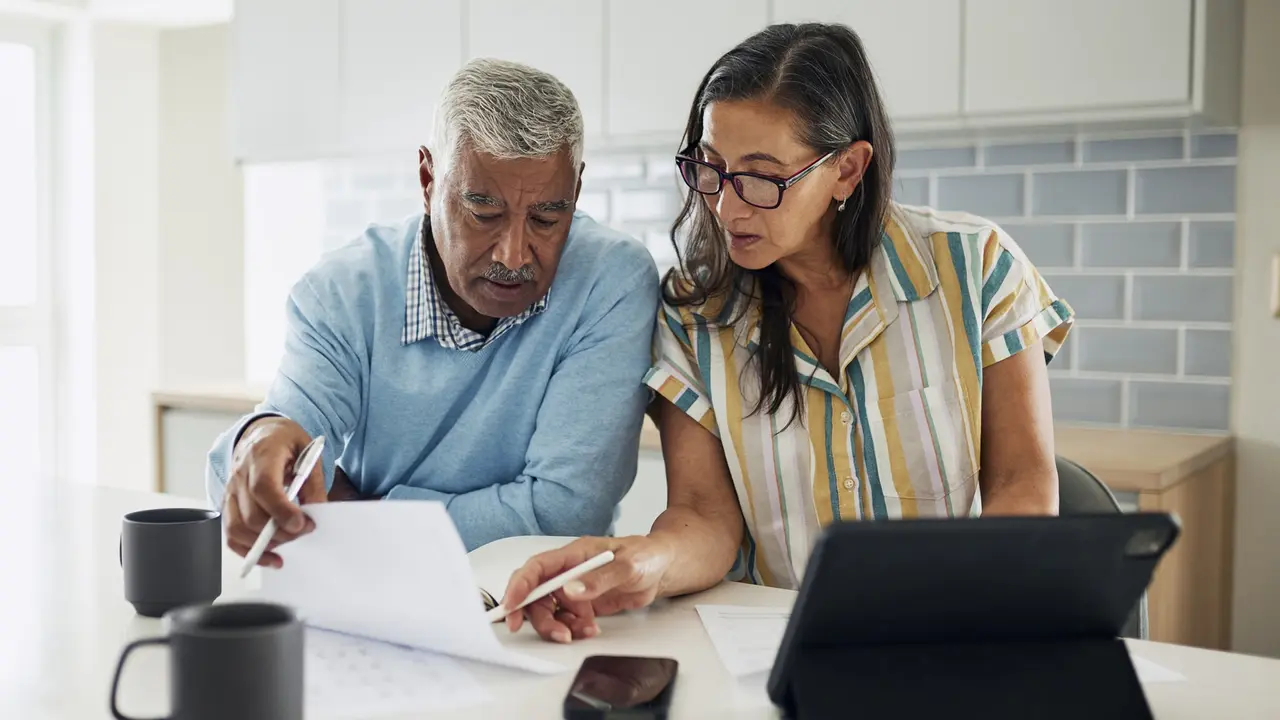 Shot of a senior couple standing in their kitchen going over finances on paper and on a tablet