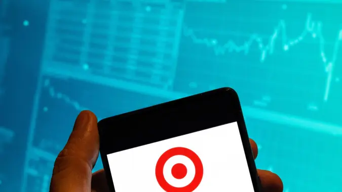 In this photo illustration, the American retail corporation Target logo is seen displayed on a smartphone with an economic stock exchange index graph in the background.