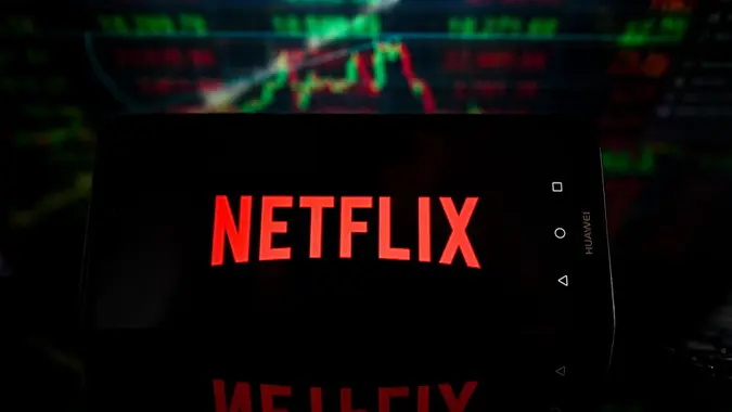 The Netflix logo is displayed on a smartphone with stock market percentages on the background.