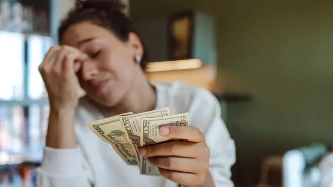 A worried woman holding a few cash bills in her home.