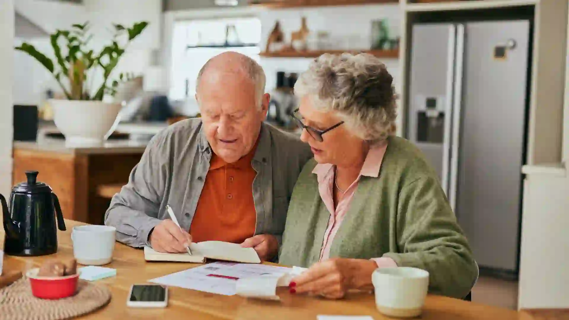 Retired couple sitting at kitchen table organizing bills and financial documents for their budget