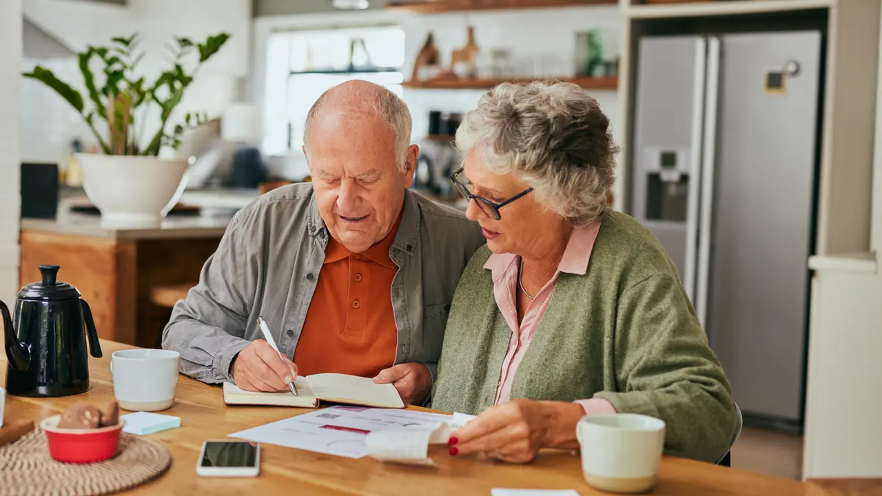 Retired couple sitting at kitchen table organizing bills and financial documents for their budget