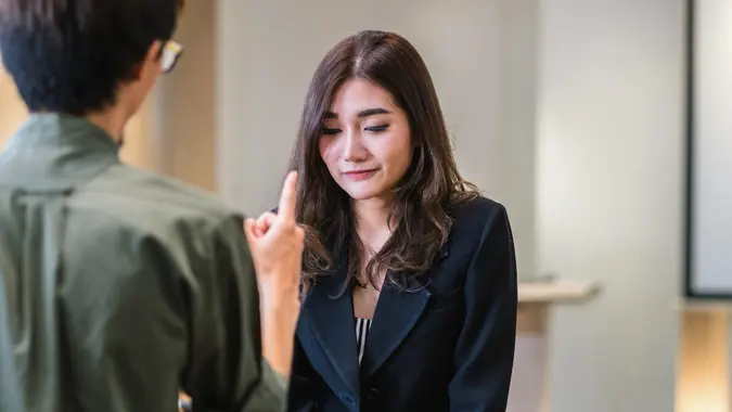 Rear view of boss scolding young young businesswoman in formal suit by point to her face in modern office, Business mistake and punish concept.