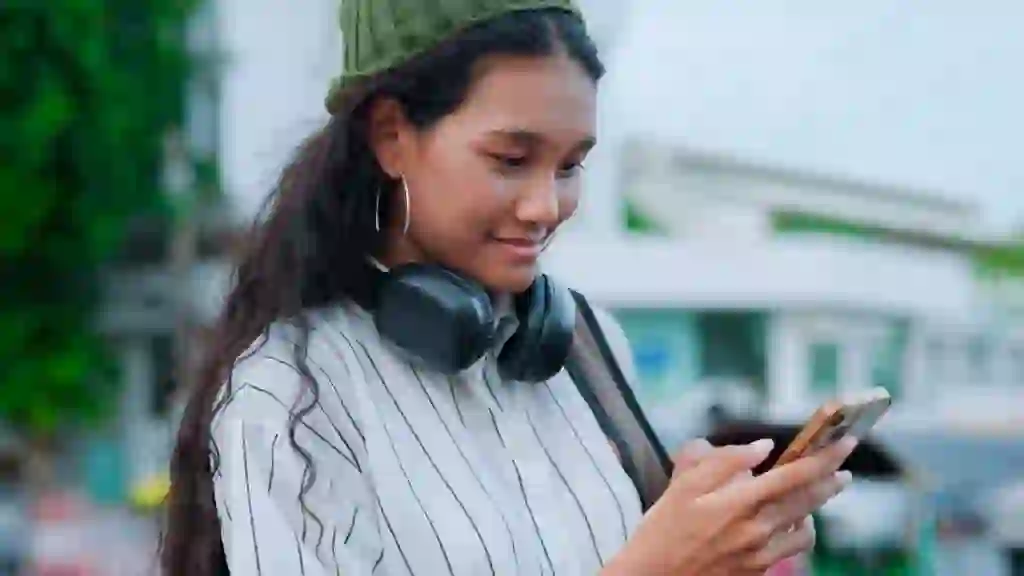 Shot of an asian woman walking outside with a wool hat and headphones and holding a smartphone