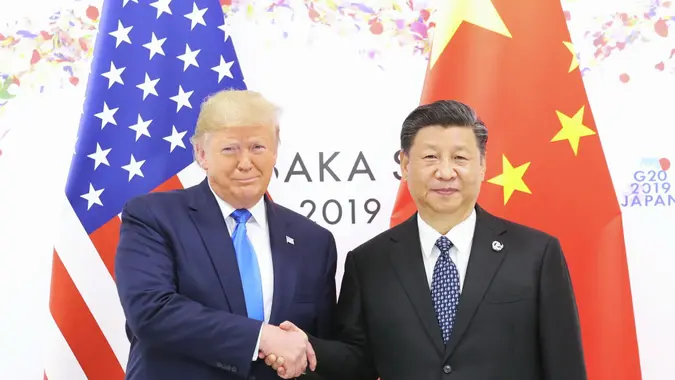 Chinese President Xi Jinping and U.S. President Donald Trump shake hands in front of the U.S. and Chinese flags.