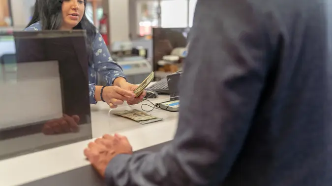Cropped shot of a female bank teller counting US Currency for a male customer at the counter in a bank.