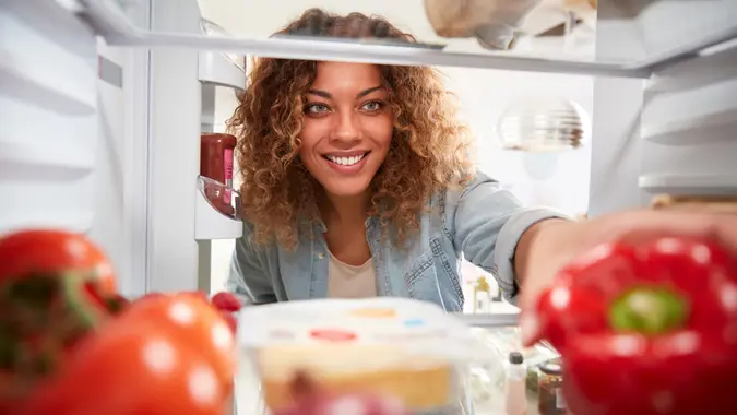 View Looking Out From Inside Of Refrigerator As Woman Opens Door And Unpacks Shopping Bag Of Food stock photo