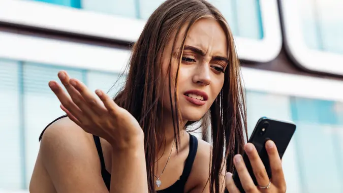 A young woman with her brow furrowed in frustration and confusion as she stares intently at her smartphone screen.