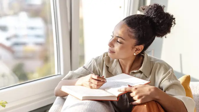 A young woman is at home, she is sitting on the sofa in the living room and writing notes
