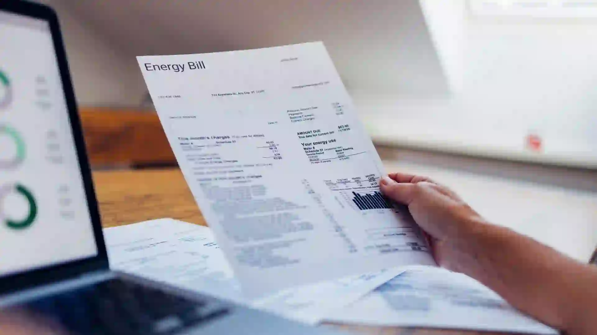 A person reviews their energy bill while using a laptop at home.