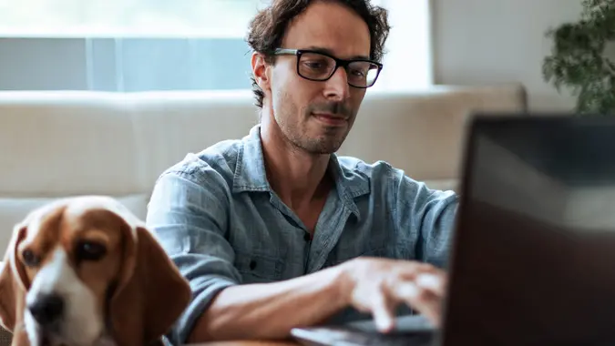 Mid-aged man comfortably working at home sitting on the floor with his Beagle dog by his side stock photo