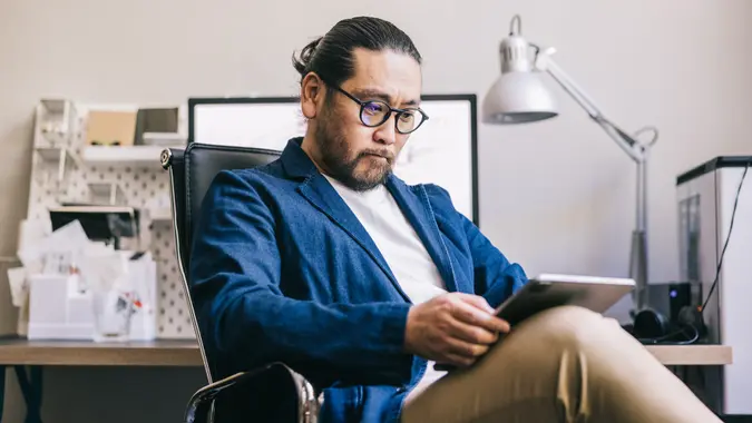 A shot of an a creative man sitting at his desk with his legs crossed and a tablet resting on one