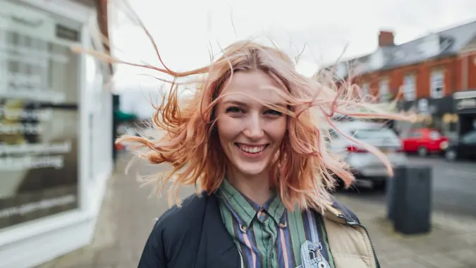 Gen Z woman with pink hair standing on sidewalk in town, smiling