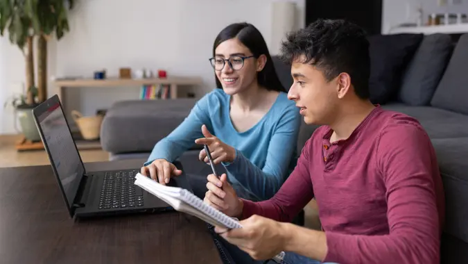 young woman and man sitting at table with laptop learning to invest