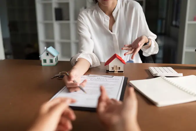 A woman is signing a document in front of a house model.