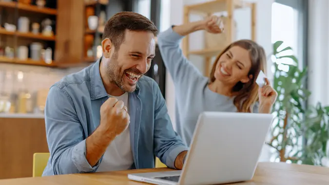 Happy couple making an online purchase using a credit card and laptop, enjoying the convenience of e-commerce.