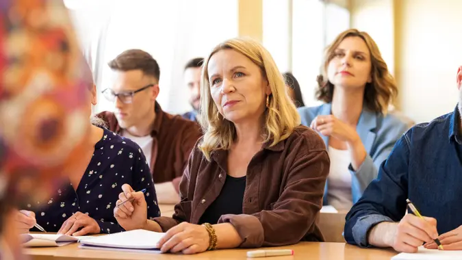 Group of adult female and male students sitting at the desks in the classroom, looking away and listening.