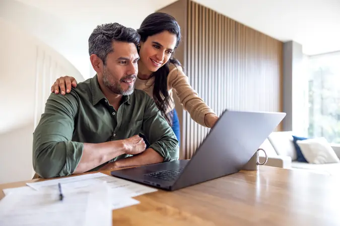 Loving couple organizing their home finances and looking at bank statements while using their laptop – financial planning concepts.