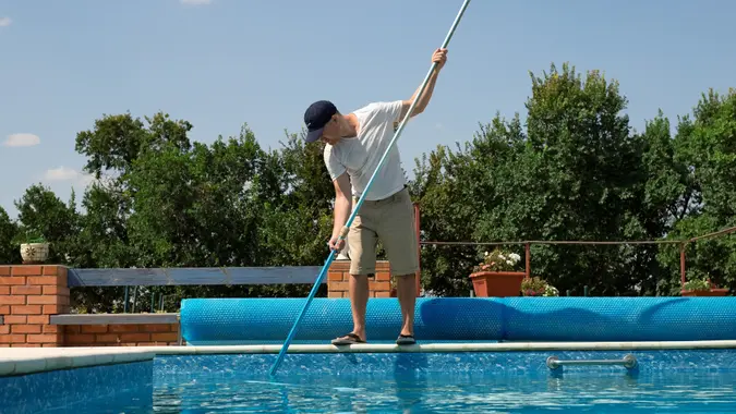 Cleaner of the swimming pool. Man cleaning outdoor swimming pool with vacuum tube cleaner in summer. Seasonal preparations.Cleaning systems for swimming pools. stock photo