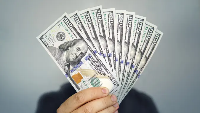 1000 dollars in 100 bills in a man's hand close-up on a dark background. Hands holding dollar cash stock photo