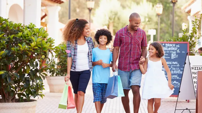 Family Walking Along Street With Shopping Bags.