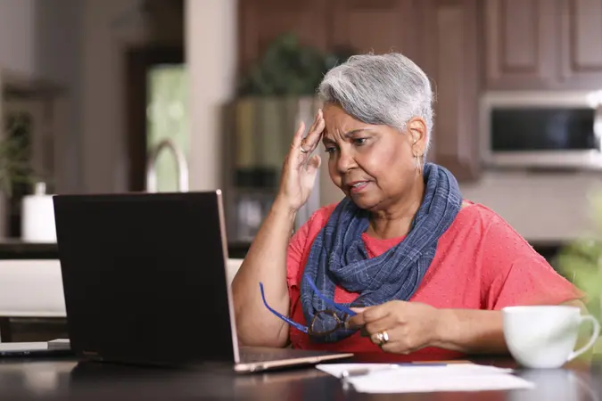 African descent, senior adult woman at home sitting at kitchen table paying bills or online banking using laptop computer.