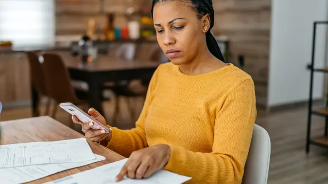 Young Woman Calculating Her Finances On A Phone At Home stock photo