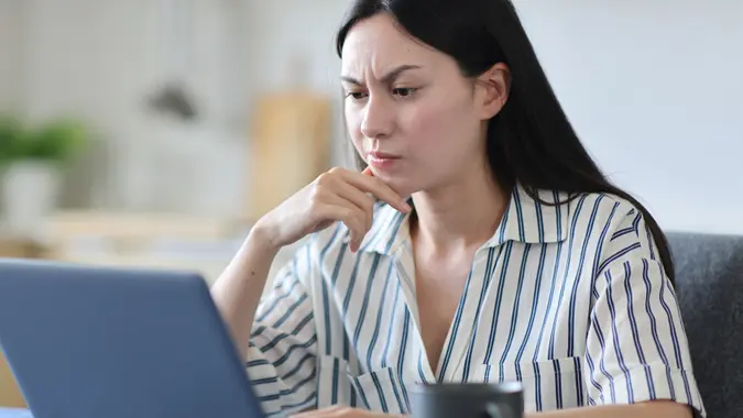 Suspicious asian woman using laptop in the kitchen stock photo
