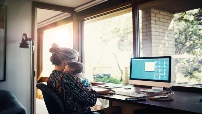 Shot of a young woman working at home while holding her newborn baby son.