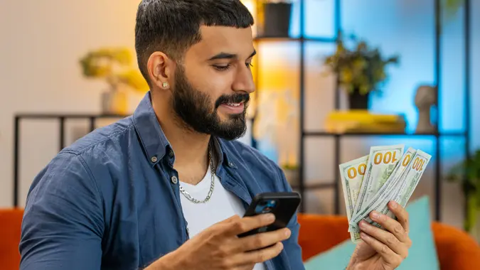 Rich Indian man freelancer using smartphone counting money cash calculate earnings at home office stock photo
