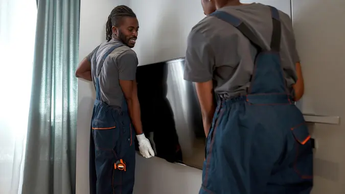Cheerful handy man and woman setting tv onto wall stock photo