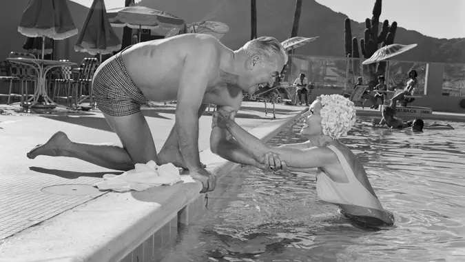 Man holding woman's hand at swimming pool, smiling stock photo