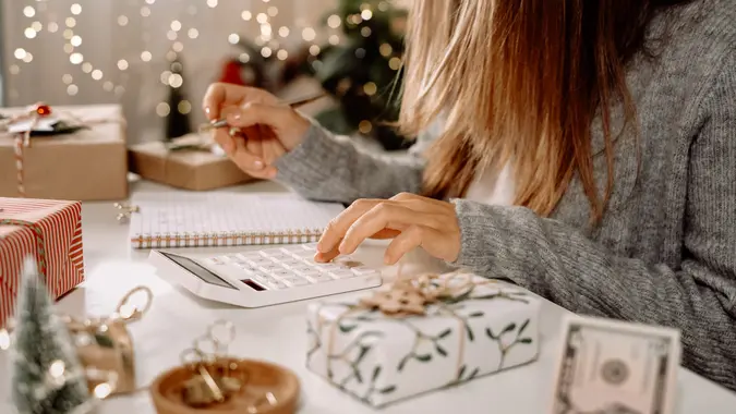 Girl counting US Dollar bills, using calculator, and writing expenses.
