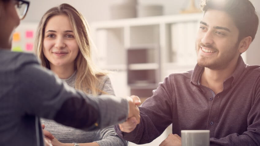 Young couple shaking hands with a female agent.