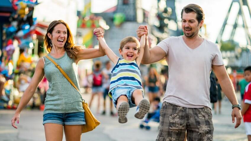 three years old boy with happy smiling mom and dad having fun on summer vacation day in themepark.