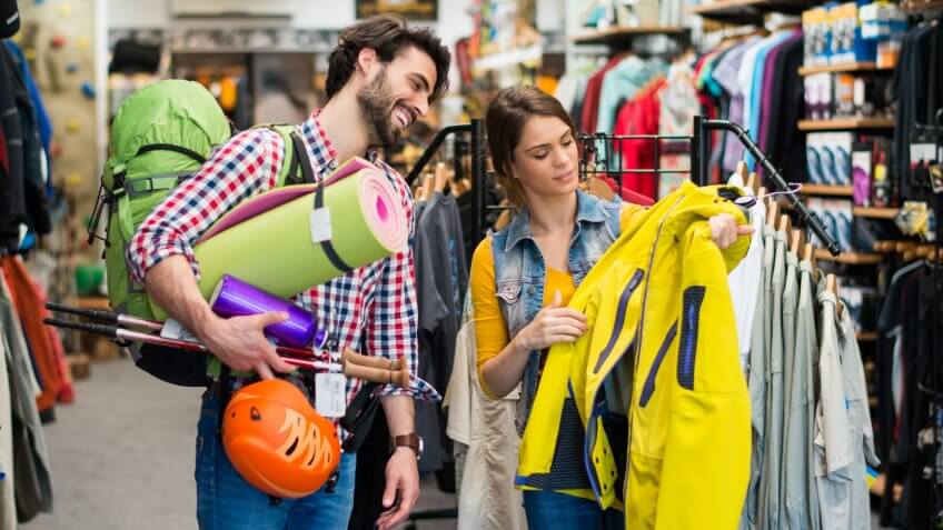 Man in sports store picking some hiking equipment, and asking a sales person about yellow jacket.
