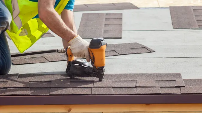 Construction worker putting the asphalt roofing shingles with nail gun on a new frame house