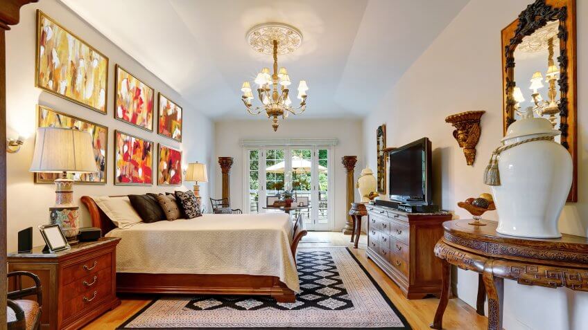 Luxury large master bedroom interior with antique carved wooden furniture, king size bed, vintage chandelier and hardwood floor.