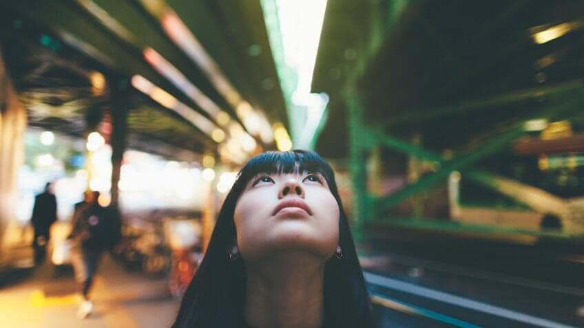 A young woman is looking up between two bridges in the city.