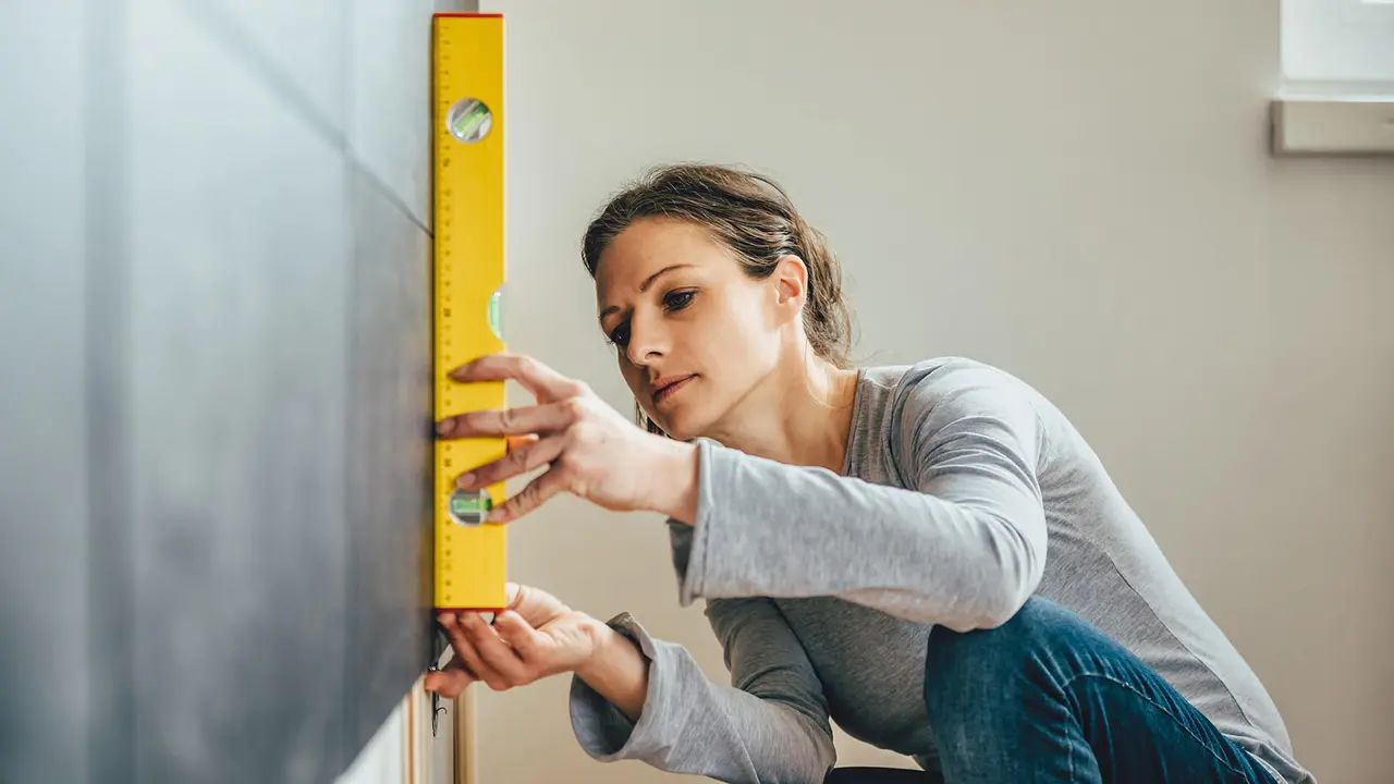 Woman wearing grey shirt using leveling tool at home.
