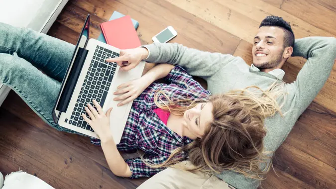 Couple shopping online at laptop computer - Two young friends watching a video on a notebook in the living room, view from above.