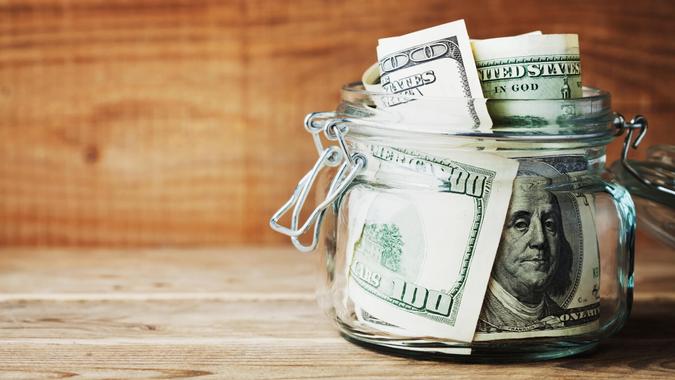 Dollar bills in glass jar on wooden background.