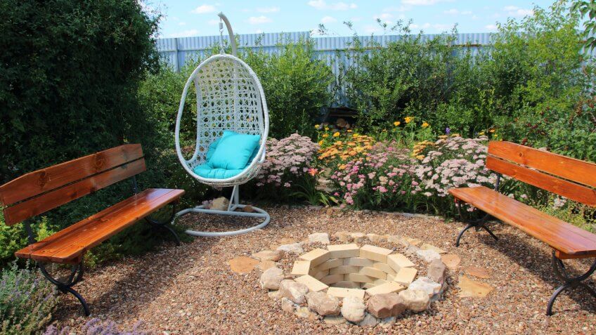 Garden rest area with a hanging swing armchair, benches and a fire pit