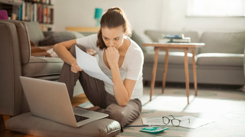 Photo of a young woman sitting on the floor and working on laptop.