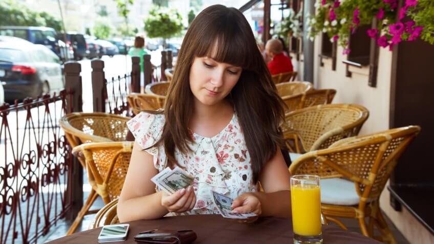 Sad woman in cafe counting money.